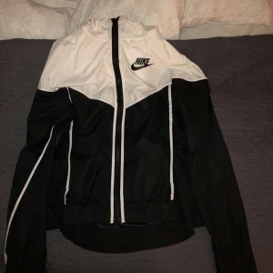 Nike windbreaker strl S vit & svart - En windbreaker jacka ifrån Nike i svart och vit. Storlek S, det är endast snöret som är lite sönder, vilket man kan fixa, annars är den i bra skick. Pris kan diskuteras!