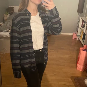 Grå flanellskjorta  - Grå, röd och blå flanellskjorta. Den är supermysig och snygg att ha över tshirts! 