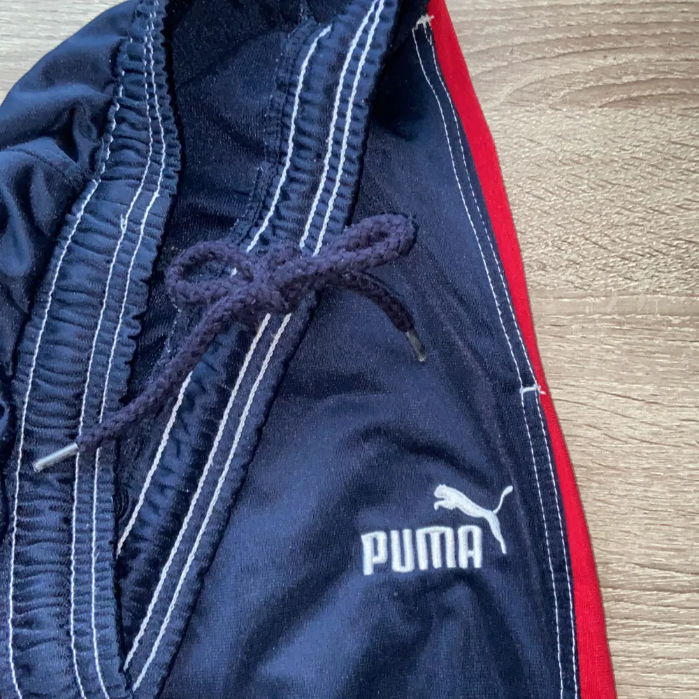 Mörkblå byxor med röd rand på sidan från Puma, justerbara i midjan. Fleece på insidan och lite glansiga i tyget på utsidan. Felfritt skick!. Jeans & Byxor.