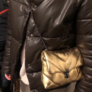 Guldig väska - Säljer min super fina guldiga väska ifrån zara. Är i bra skick men använd flitigt, inget är trasigt men kedjan har tappat lite färg på vissa ställen och även på spännet, men det är ingenting man tänker på. Den är helt slutsåld och finns inte längre att köpa 💕buda privat från 250kr 