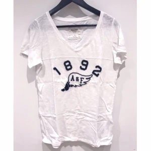  - T-shirt från Abercrombie&Fitch, vit med navy text och V-ringning. Passar en S/M, även XS som lite lösare modell.