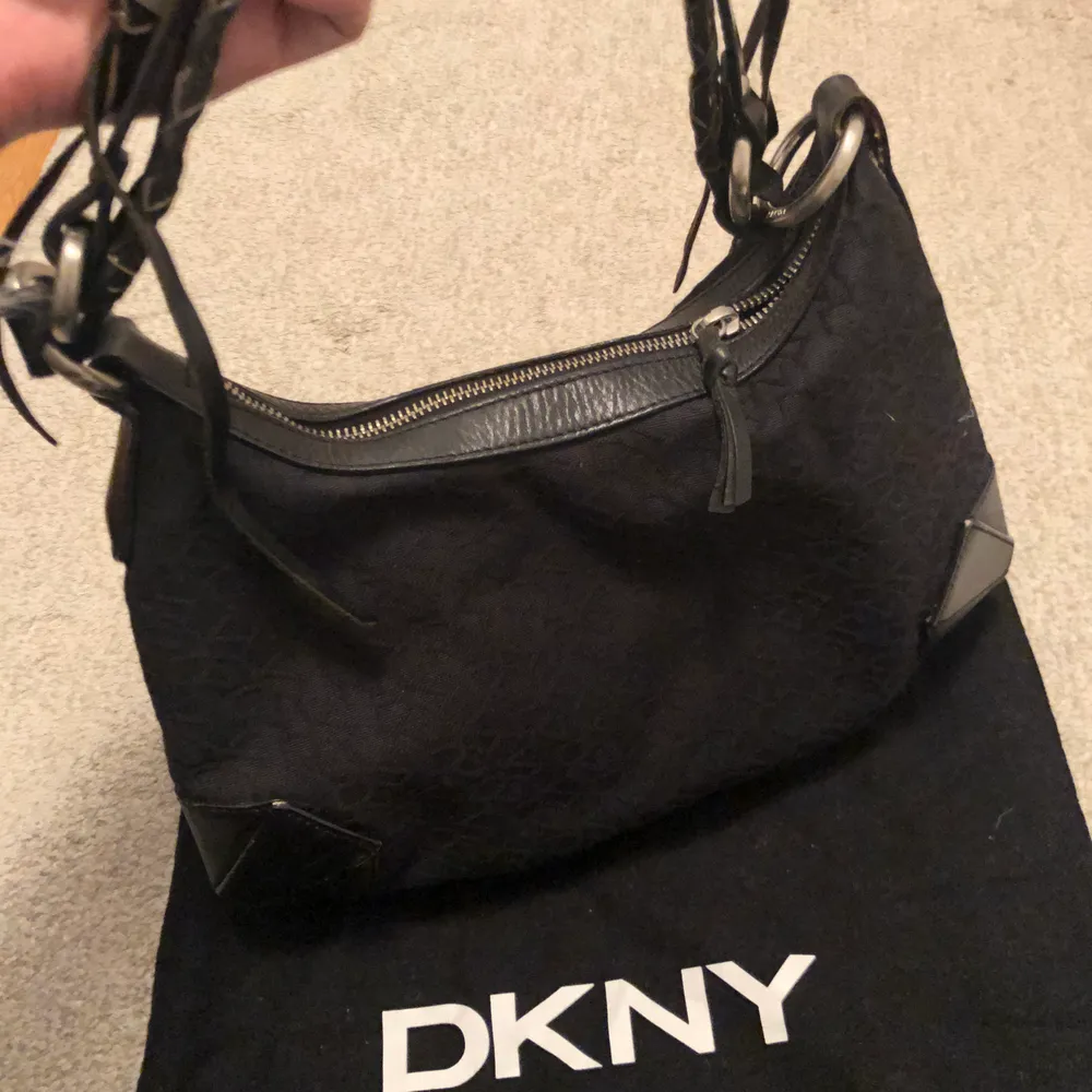 Äkta DKNY handväska, klassisk svart med embossed loggan och snygg flätad rem med detaljer. Kan postas eller mötas upp 📮😊. Väskor.