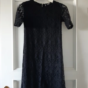 Kort svart klänning  - I broderat material. Svart undertyg. Som ny, endast använd 1 gång!