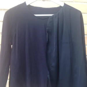  - Mörkblå stickad tröja från COS med halva framsidan i silkigt material. Lite tight i ärmarna men kan nog användas som S eller M. Går att handtvätta. 100% merinoull och 100% polyester. Fint skick!