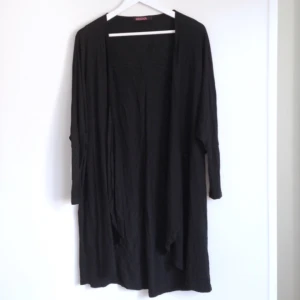  - Svart långkofta i mjukt tyg. Litet längre baktill och snygga ärmar. Fint skick!
