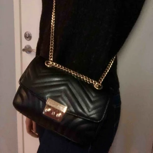 Väska från Nelly - Snygg väska från Nelly i nyskick med guldiga detaljer! Mkt sparsamt använd. Väldigt rymlig trotts att den är rätt så liten (Iphone för skala). Hela väskan är ca 20 cm i bredd och 13 cm i höjd och är gjord i fejkläder. Köparen står för eventuell frakt 🥰