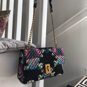  - Blommig axelremsväska från Mango! Använd fåtal ggr och i mycket gott skick! Kedja och detaljer i fin guldfärg. Svart botten med färgglada blommor. I blank tyg. Mindre innerfack och ljust foder invändigt. Ett litet märke på ens hörnet (undertill) där trådarna har börjat trispa upp sig lite, i övrigt jättefint skick! Nypris 800:- (18x28x7cm)  Betalas lättast genom swish el överföring till konto, skickas med posten för 49:- (köparen betalar frakten)