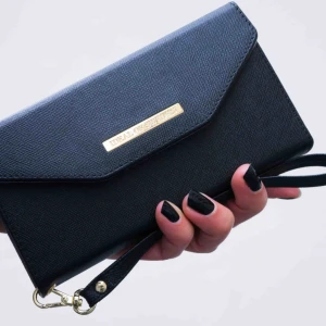  - Smart mobilplånbok med plats för 3 kort och sedelfack. Mayfair Clutch, designad som kuvertväska med handledsrem. Svart läderimitation. Passar alla mobilskal från iDeal of Sweden då dessa är magnetiska fäster de direkt i denna funktionella plånbok.