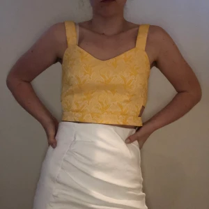 Topp i jaquard-mönster - EJ TILLGÄNGLIG JUST NU Gul topp i jaquardmönster i storlek M, aldrig använd. Dragkedja baktill. Slutar strax ovanför naveln. Passar bra till vit kjol eller vita kostymbyxor. Köparen står för frakt, standardfrakt 63 kr med postnord. Betalning sker via swish. Inga returer. 