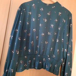 H&M blus i strl 44 - Supersöt blus från H&M. Bilderna gör inte färgen på blusen rättvis, den är en mörk skogsgrön färg. Jag har använt den 1 kanske 2 ggr, men den är förliten runt bysten på mig. Kan mötas upp eller skicka, jag står INTE för frakten