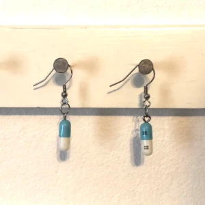 Örhängen med tabletter - Söta örhängen med blåvita tabletter på. Kapslarna är äkta men jag har tagit ut medicinen som har varit inuti. Det står små söta siffror på sidan av kapslarna. Kontakta mig om du har några frågor så svarar jag gärna 😊