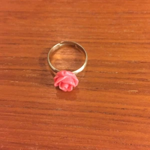 - Rosa ring med ros på. Själva ringen är ställbar och kan anpassas efter storleken på fingret. 