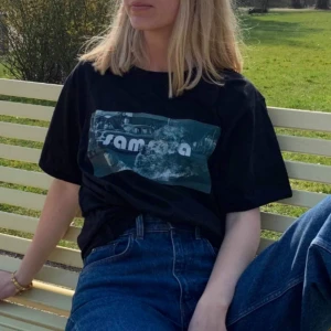  - Vintage svart t-shirt med nytryckt design!                    SAMSARA köper in secondhand kläder som inte blir sålda och revitaliserar dem med unika och högkvalitativa tryck. Varje plagg sparar cirka 2400L vatten och 1,4 kg co2!  Modellen är 165cm!