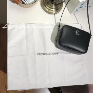 Ckalvin Klein (jeans) Axelremsväska - En svart fin ny axelremsväska från CKJ (äkta se bild p ”kvittot” eller vad man kallar det, mappen med bevis i alla fall) Fin och så men har inte använt på länge och behövde rensa. Den är som sagt ny och använd 2 ggr. Köptes från CK hemsida se bild på CK-mappen. Köptes för 900kr och är i nyskick, har inga som helst märken och är som ny. Kan frakta och kanske mötas. Ni kan få flera bilder om ni vill det är bara att fråga! Alla bilder fick ej plats här. (Fråga om du vill veta fraktpris oxå)