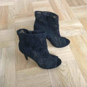  - Svarta oanvända klackar i fint mönster! Klackhöjd ca 10 cm. Sååå fina men kommer inte till användning!  Dragkedja på insidan 