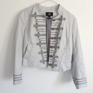  - Ljusgrå orkesterjacka från H&M med fina detaljer 👑 Använd men i fint skick. Modellen är midjekort! Passar även dig som är en 36a. Frakt 49kr Jag har svish 💸💸