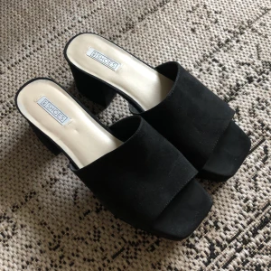 Slip-ins i mockaimitation - Slip-ins med klack och platå i svart mockaimitation, endast avvända 1 gång inomhus. Litet märke på insidan av ena klacken som inte syns vid användning. Frakt ingår.