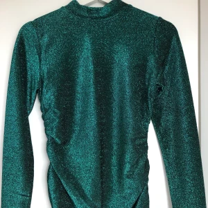 Glittergrön topp - Använd 1 gång! Superhärlig glittrig topp som går upp i halsen och är lite ribbad i sidorna. Tight passform. 