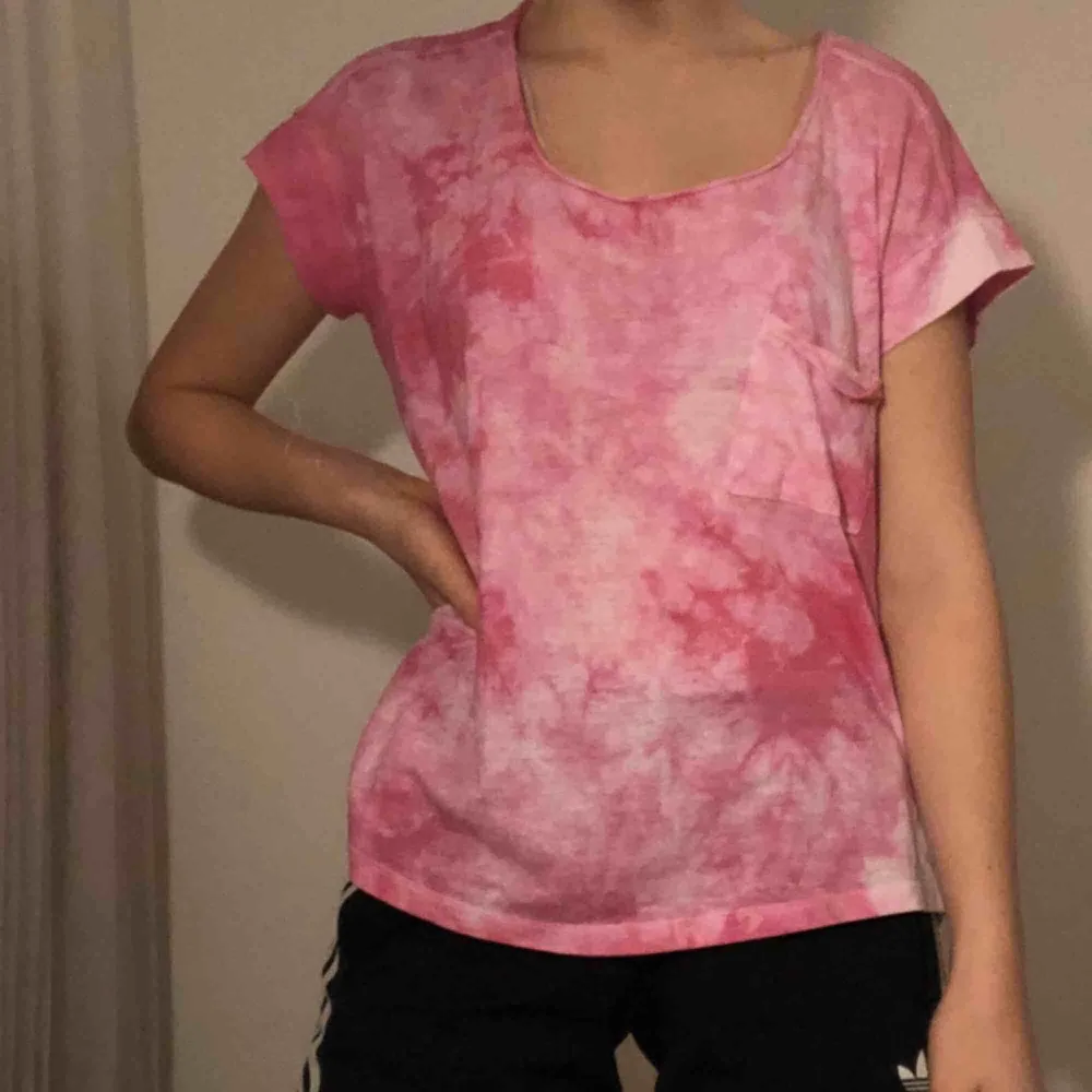 Rosa T-shirt med batikmönster och en ficka vid ena bröstet. Möts i Stockholm annars betalar köpare frakt. . T-shirts.