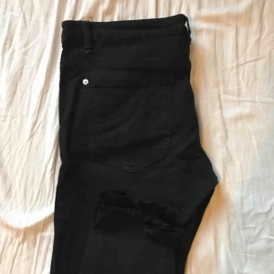 Svarta jeans med hål i knäna - Svarta tighta anklejeans från Pull&Bear. Har slitningar vid ankeln och hål vid båda knäna. Jättefina basic jeans med normal midja. Har ingen stretch så därför skulle jag säga att storleken är mer som M.