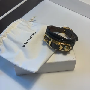 Balenciaga armband  - Ett mörkblått Balenciaga armband med gulddetaljer inköpt 2018 i Paris. Dustbag tillkommer vid köp. Armbandet är använt ett få tal gånger och är i mycket fint skick. Säljes för 600 kr.