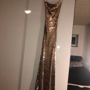 Klänning strl S - Aldrig använd, stretchigt material. Öppen rygg med korsande snören som knyts. Slit på vänstra benet och ryschat tyg vid svanken. Strl S men stretchar. Lång!