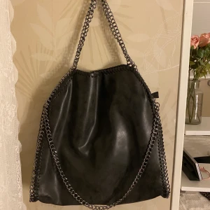 Mörk grå väska med kedjor!! - En fin och rymlig mörk grå väska med kedjor, kommer inte till användning därav säljer jag den😀 Den har dragkedjan  och även små fack i väskan. Lik Stella McCartney väskan:) 100kr+ frakt