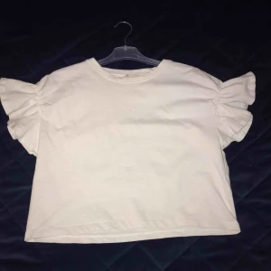  - Jättesöt kortare t-shirt med volang på axlarna. Supersnygg till högmidjade byxor eller på sommaren till en kjol. Tycker denna är så fin att ha istället för en vanlig vit t-shirt! Storlek 38