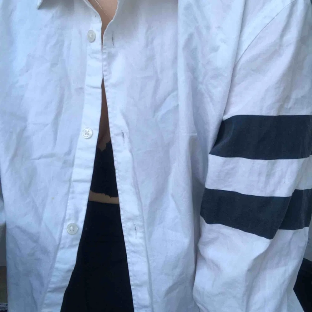 Snitsnygg vit skjorta med marinblåa ränder på ärmarna. Använd en del men fortfarande i bra skick!. Skjortor.