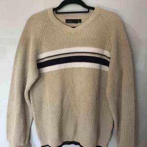  - Jättefin beige tröja med linjer på bröstet. V-ringning i halsen och mörkblå linjer vid ärmslut. Köpt på second hand. Säljes då plagget tyvärr inte längre är min stil! Frakt tillkommer:)