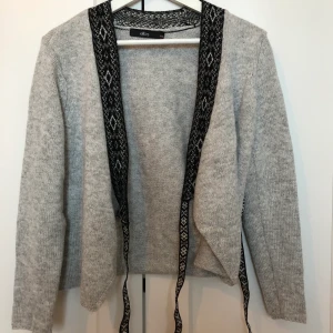 Stickad tröja - Stickad tröja ifrån Ellos som är grå med svarta detaljer, plagget är endast använt fåtal gånger och är i fint skick. Köparen står för frakt 69kr