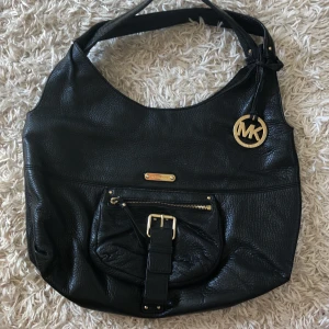 Michael Kors väska - Svart läderväska med gulddetaljer från Michael Kors. Rymlig med många fickor både i och på. Inköpt i USA. Nypris ca 2000kr. Gulddetaljerna har blivit lite repiga pga slitage därav det otroligt billiga priset. Köparen står för frakt.
