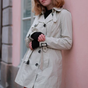 Trench coat - Beige trenchcoat från Cubus strl 36. Använd men inga defekter. Har fickor på sidorna och går inåt i midjan.Jag på bilden är 164 och den blir nog lite kort på någon som är mycket längre än mig. Köpare betalar frakt, går annars att hämta eller mötas upp. 