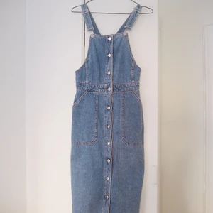 Jeansklänning - En härlig jeansklänning med hängslen som formar och framhäver en fantastisk midja. Relativt lång som går en bit nedanför knäna. 