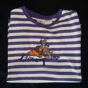 Vintage Disney Lady&Lufsen T-shirt - Så söt broderad vintage Lady&Lufsen T-shirt med vita och lila ränder! Från 90-talet och går inte att få tag på längre, likadana har sålts på ebay för många hundra kronor så den har troligen ett samlarvärde! Den sitter lite oversize på en S :)