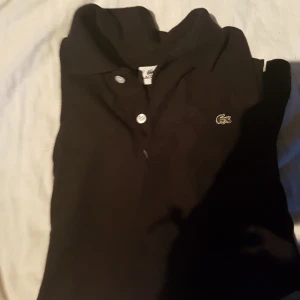  - Svart lacoste piké i storlek small , köparen står för frakt  Förlåt för dålig bild 