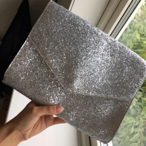  - Glittrig kuvertväska med silvrigt Band (går att vika ner i väskan och ha den som en clutch) från H&M, knappt använd i jättefint skick.