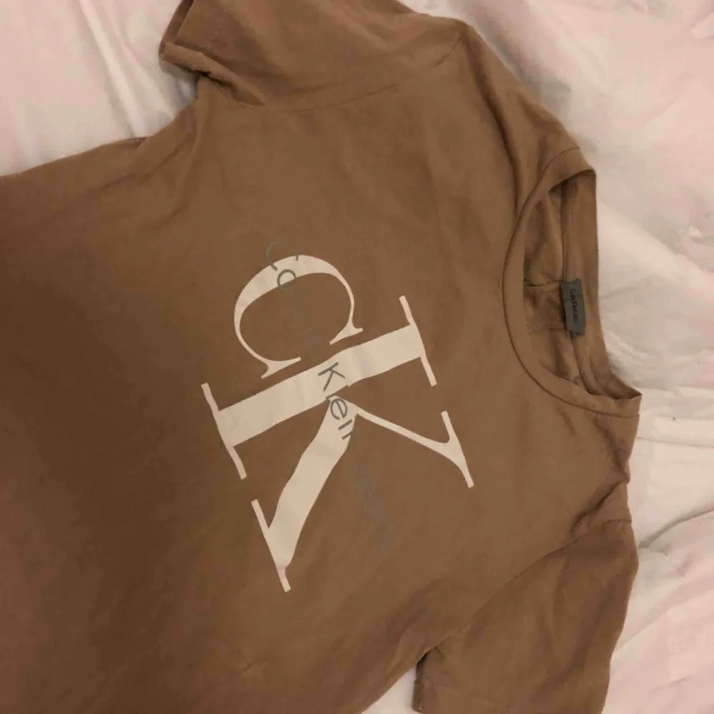 Beige/brun t-shirt från Calvin Klein, max använd 2 gånger så helt i ny skick. Snyggt tryck på bröstet och dom klassiska dubbla sömmarna i ryggen.. T-shirts.