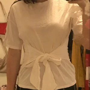 vit t-shirt med detaljer  - vit t-shirt med detalj på ärmarna och knytdetalj över midjan. köpt från monki. i gott skick. 