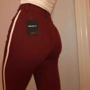 Forever 21 jeans - Helt oanvända röda jeans ifrån Forever 21. En jättefin mörkröd färg med ett vit streck på vardera sida. Stretchigt material med en slits längst ner. På gränsen för korta för mig som är 173. I nyskick. Skriv om du undrar något! :)