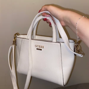 Vit guess väska - Säljer denna fina vita (fake!!!) guess väskan med guldiga detaljer. Superfin med två olika sätt att bära på och bandet är justerbart! Passar till allt men har så många väskor så kommer ej till användning :((💕💕💕💕