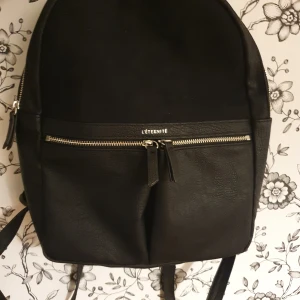 Väska - En mindre ryggsäck med präglad läderimitation med parti i mockaimitation framtill.   Använd en gång!  Djup: 9cm Bredd: 23cm Höjd: 31cm | Bud startar från 100kr och måste höjas med 50kr