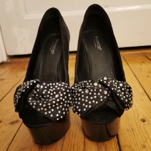 Klackar bianco - Bra skick. 13 cm klack med platå framtill och öppen tå. Strassrosett över foten. Ger en otroligt smickrande fotrygg. 