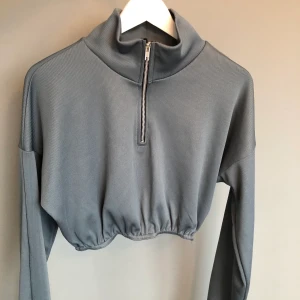 Långärmad magtröja Prettylittlething  - Supersnygg grå kort tröja i ribbstickning med dragkedja framtill. Använd 1 gång, Mkt bra skick. Köpt för 300kr på Asos (slutsåld).