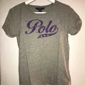 Grå t-shirt från Ralph Lauren med ett lila Polo tryck på magen. Storlek XS, ganska liten i storlek. Använd ett fåtal gånger.