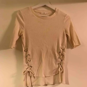  - En creme-färgad tröja med snören vid sidan om. 