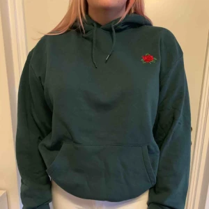  - En mörkgrön hoodie med en ros på vänster bröst, från hm. Frakt tillkommer