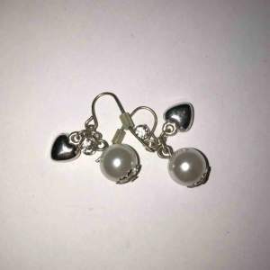 Ett par hängande örhängen med en vit pärla, ett hjärta och en kristall. Helt oanvända. Köparen betalar frakten