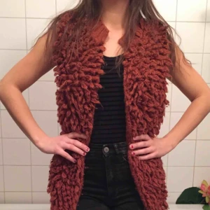  - Lurvig väst i rostrött Längre fram, kortare bak. Akrylgarn, så sticks ej Porto tillkommer