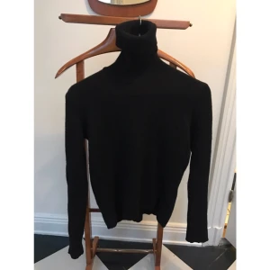  - Svart polotröja från Carin Wester. 70% ull, 30% yak (endast handtvätt). Kortare modell med slitsade armar och mindre slitsar på sidorna. 